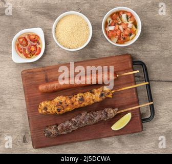 Spiedini di carne, pollo e salsiccia di maiale su tavola di legno con farofa e vinaigrette. Foto Stock