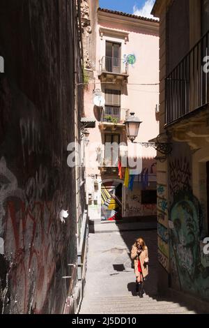 Giovane donna che parla al telefono / cellulare / telefono / camminando in salita affondata di scalini su Via Penninello, Città di Catania, Sicilia. Italia. Vista da Via Crociferi. (129) Foto Stock