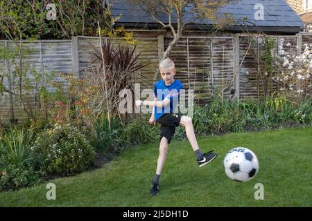 Ragazzo caucasico di 11 anni che gioca a calcio nel giardino posteriore, Inghilterra, Regno Unito Foto Stock