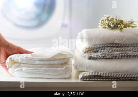 Persona che utilizza lavanderia self-service per il pubblico con biancheria da letto e personale su una panca bianca e lavatrice professionale in background. Vista anteriore Foto Stock