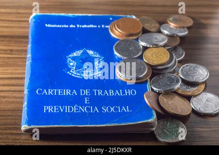 Traduzione: Repubblica Federativa del Brasile, Ministero del lavoro. Scheda di lavoro (Carteira de trabalho) accanto alle monete reali brasiliane, denaro brasiliano. Foto Stock