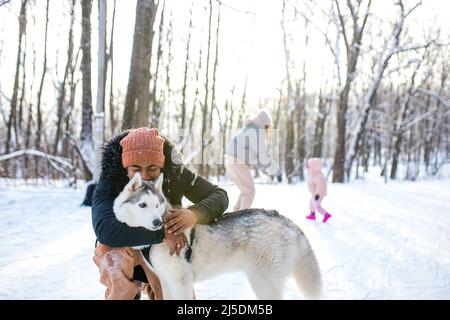 l'uomo misto di gara abbraccia il suo cane husky nel parco forestale invernale Foto Stock