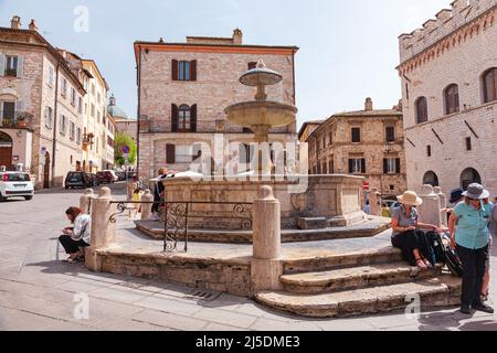 Antica fontana e gente in Piazza del comune della cittadina di Assisi, Umbria, Italia. Turisti in una piazza ad Assisi. Foto Stock