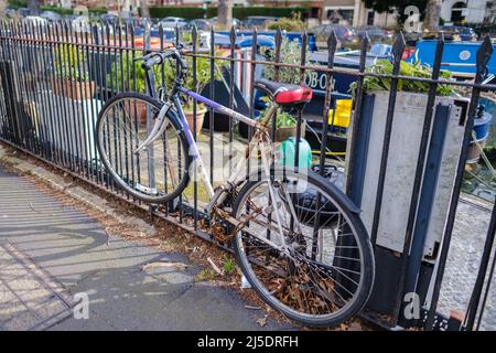 La bicicletta di un uomo è incatenata alla recinzione di Blomfield Rd., accanto al Regent’s Canal, Little Venice, Londra, Inghilterra. Barche a remi e case sullo sfondo. Foto Stock