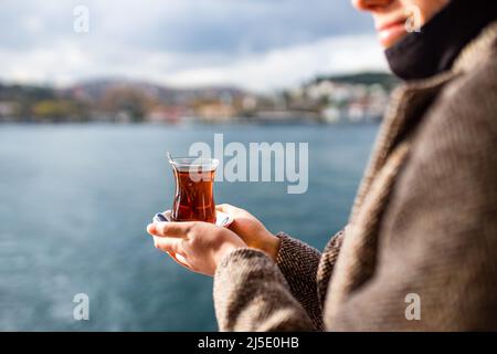Donna che beve il tè turco nella parte anteriore, baia bosforo in background Foto Stock