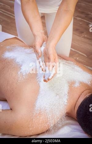 Una donna guaritrice esegue un rituale con sale, versa il sale sulla schiena di un uomo menzogna. Relax. Foto Stock