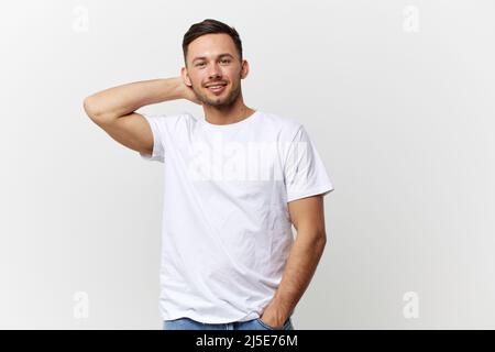 Sorridente felice goduto giovane abbronzato bell'uomo in t-shirt base tenere la mano dietro la testa posando isolato su sfondo bianco studio. Spazio di copia Foto Stock