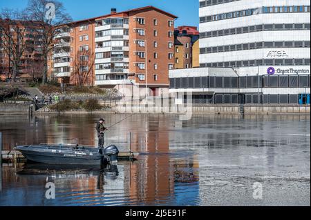 Uomo che pesca nella città di Norrköping a Refparens grund del fiume Motala in una soleggiata primavera nel mese di aprile 2022. Norrkoping è una città storica della Svezia. Foto Stock