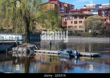 Uomo che pesca nella città di Norrköping a Refparens grund del fiume Motala in una soleggiata primavera nel mese di aprile 2022. Norrkoping è una città storica della Svezia. Foto Stock