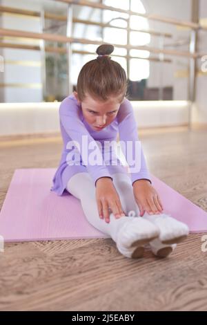 Adorabile foto di ballerina in abito lilla e collant bianco esercizi di stretching in una sala con grandi specchi. Foto Stock