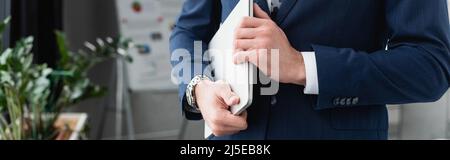 vista ritagliata dell'uomo d'affari in blu blazer che tiene il laptop in ufficio, banner Foto Stock