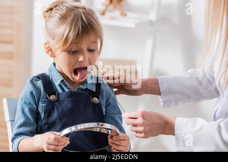 Ragazza che tiene lo specchio vicino al terapeuta del parlato con sonda logopedica in aula Foto Stock