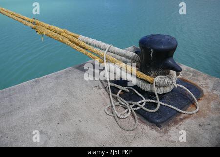 Nave Bollard con le linee di ormeggio attaccate montate su un bacino di cemento dall'oceano Foto Stock