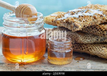 Primo piano di miele delizioso che gocciola da nido d'ape freschi su vaso di vetro con bastone di legno del divipper del miele su vecchio tavolo di legno. Sano biologico natura hon Foto Stock