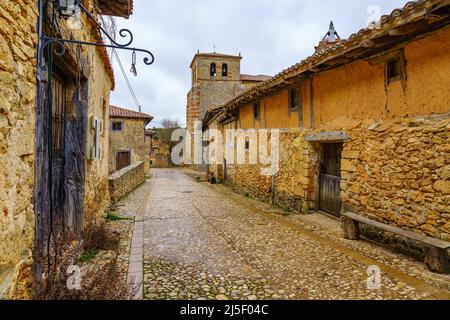 Vicolo stretto del borgo medievale e la sua chiesa sullo sfondo, Calatanazor, Spagna. Foto Stock