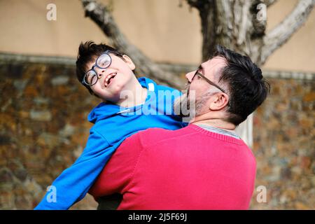 Amorevole padre che tiene e gioca con il figlio disabile mentre si gode il tempo insieme all'aperto. Foto Stock