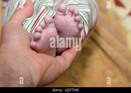Un padre tiene il piede del bambino, le dita dei piedi del neonato in mano del genitore, i piedi del bambino neonato sul palmo del padre su uno sfondo sfocato, parenting, pazzi Foto Stock