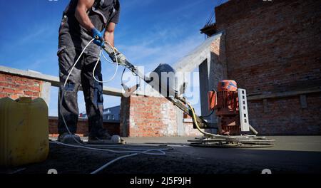 Vista laterale del lavoratore in speciale lavoro uniforme con attrezzature in costruzione. Concetto di processo di preparazione dei lavori per la costruzione di pareti in buone condizioni climatiche estive. Foto Stock