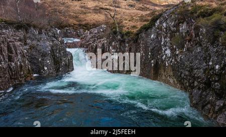 Splendida immagine aerea del paesaggio dei droni del vibrante fiume Coe che scorre sotto le montagne innevate nelle Highlands scozzesi Foto Stock