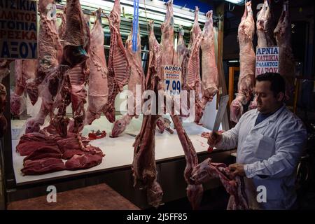 Atene, Grecia. 21st Apr 2022. Un macellaio è visto tagliare la carne in pezzi più piccoli come agnelli macellati interi e capre sono appesi pronti per la vendita nel famoso mercato alimentare di Varvakios per il tradizionale pasto pasquale spit-arrostito. L'aumento dei prezzi ha colpito la delicatezza tradizionale greca preferita. (Credit Image: © Dimitris Aspiotis/Pacific Press via ZUMA Press Wire) Foto Stock