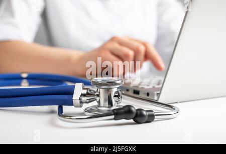 Medico seduto al tavolo con computer portatile e stetoscopio. Trattamento online dei pazienti. Utilizzo del computer per il lavoro in ospedale. Foto di alta qualità Foto Stock