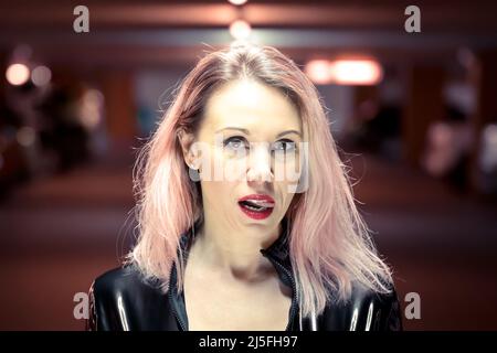 Primo piano ritratto di bella giovane donna con capelli tinti indossando giacca in pelle che sporge lingua in garage illuminato parcheggio Foto Stock