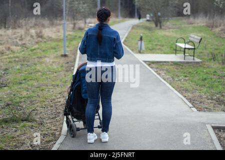 Una donna con un passeggino cammina nel parco. Una madre cammina un bambino piccolo. La ragazza è in piedi sulla strada del parco. Foto Stock