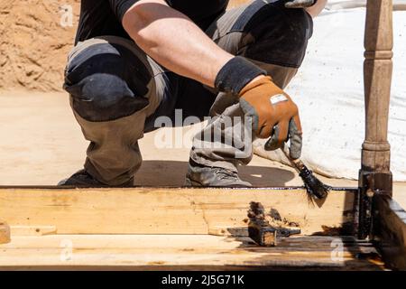 Uomo che lavora al restauro di mobili antichi utilizzando bitume judaicum. Cura del legno e concetto di impermeabilizzazione Foto Stock