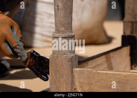 Uomo che lavora al restauro di mobili antichi utilizzando bitume judaicum. Cura del legno e concetto di impermeabilizzazione Foto Stock