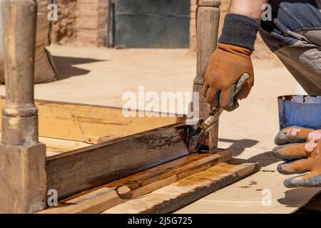 Uomo che lavora al restauro di mobili antichi utilizzando bitume judaicum. Cura del legno e concetto di impermeabilizzazione Foto Stock