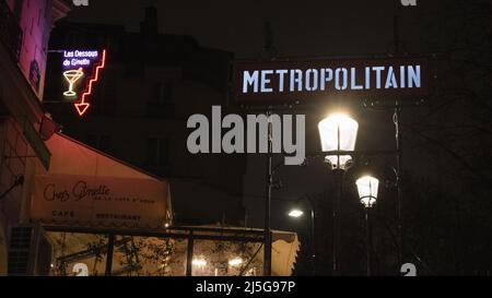 Parigi, Francia: Vista notturna, lampioni di strada e segni al neon all'ingresso della stazione della metropolitana di Montmartre, famosa collina nel nord 18th ° arrondissement Foto Stock