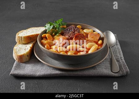 Ricetta tradizionale di fagioli con chorizo e salsiccia di sangue di Fabada Asturiana su un tavolo scuro. Fuoco selettivo Foto Stock