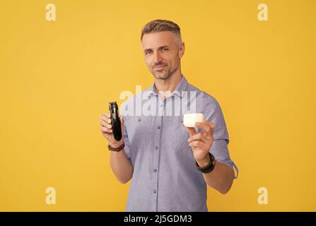 barbiere. dopo la rasatura. l'uomo tiene il rasoio elettrico e la crema. il ragazzo grizzled presenta il rasoio elettrico Foto Stock