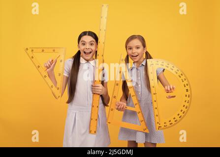 Torna a scuola è qui. Le ragazze felici tengono gli attrezzi geometrici. Ritorno a scuola. Lezione sulla geometria Foto Stock