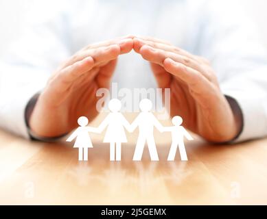 Concetto di assicurazione di famiglia con carta famiglia cutout coperto da mani Foto Stock