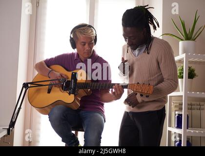 Un tutor afroamericano personale spiega al suo studente asiatico come giocare accordo studiato correttamente. Educazione musicale a casa Foto Stock