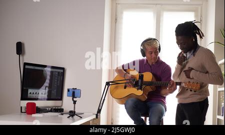 Un tutor afroamericano personale spiega al suo studente asiatico come giocare accordo studiato correttamente. Educazione musicale a casa Foto Stock