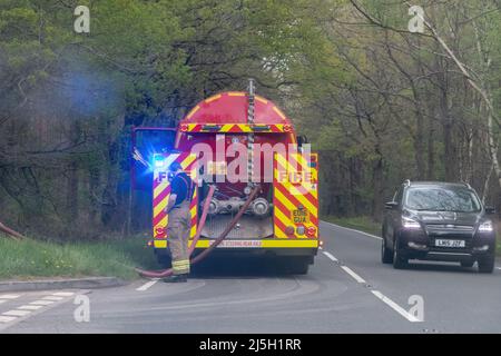 Ceneri, Surrey, Inghilterra, Regno Unito. 23rd aprile 2022. Un grande fuoco di brughiera è scoppiato su Ash Ranges, che una riserva naturale heathland ovest di Pirbright in Surrey. È di proprietà del Ministero della Difesa e gestito dal Surrey Wildlife Trust. Un vigile del fuoco e un motore antincendio su una strada di campagna vicino al sito che lavora per aiutare a spegnere il fuoco. Foto Stock