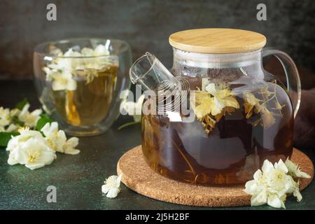 Tisane terapeutiche. Tè verde caldo con fiori di gelsomino in una teiera di vetro su un tavolo di pietra. Foto Stock