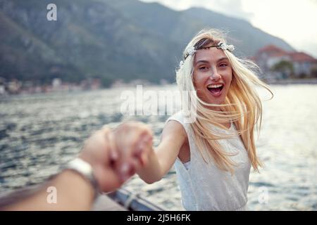 Bella sposa bionda allegra con corona floreale in capelli tenendo i suoi uomini per mano. Coupé in luna di miele. Matrimonio, luna di miele, concetto di amore Foto Stock