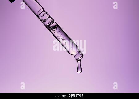 Primo piano una pipetta cosmetica con essenza e una goccia chiara su sfondo viola. Colore dell'anno 2022 primo piano con caduta Foto Stock