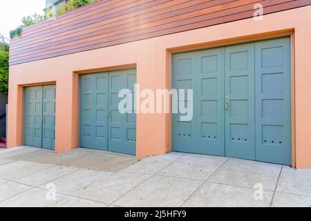 Tre porte da garage con cerniera laterale e maniglie in oro a San Francisco, California. Garage esterno sotto la recinzione in legno con piante sopra. Foto Stock