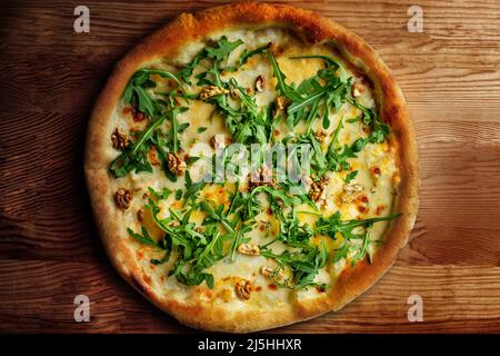 Deliziosa pizza al formaggio vegeteriana con noci e basilico sullo sfondo del tavolo in legno, vista dal primo piano Foto Stock