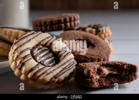 Biscotti alla vaniglia ripieni di crema di cioccolato su un piatto bianco su un tavolo di legno bianco e una parete di legno sullo sfondo Foto Stock