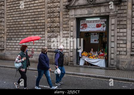 Barcellona, Spagna. 23rd Apr 2022. Una donna con un ombrello rosso ha visto camminare oltre una bancarella che vende rose durante il giorno di Sant Jordi. Il tradizionale giorno dei libri e delle rose che si celebra in Catalogna per commemorare il giorno di Sant Jordi ha sofferto questo anno con forti piogge e grandine. Credit: SOPA Images Limited/Alamy Live News Foto Stock