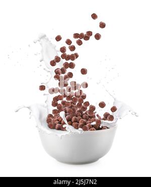 Versare le gustose palle di mais al cioccolato nella ciotola con spruzzi di latte su sfondo bianco Foto Stock