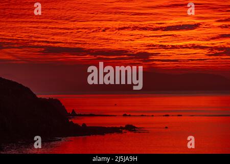 Tramonto rosso sullo stretto di Cook, da Titahi Bay, Porirua, Wellington, Isola del Nord, Nuova Zelanda. South Island in lontananza. Foto Stock