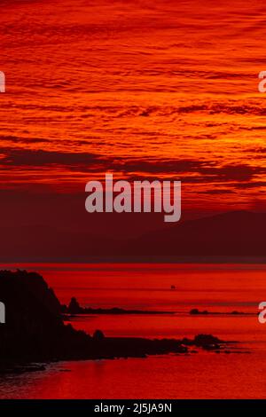 Tramonto rosso sullo stretto di Cook, da Titahi Bay, Porirua, Wellington, Isola del Nord, Nuova Zelanda. South Island in lontananza. Foto Stock