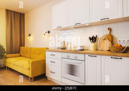 piccolo monolocale con divano giallo, cucina bianca. Luce accogliente accesa Foto Stock