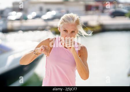 Donna più anziana che fa boxe ombra all'aperto. Donna anziana che fa sport in un porto costiero Foto Stock